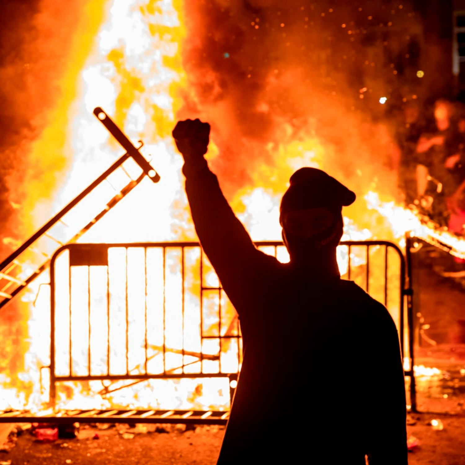 Masked protester raising fist in front of burning barricade during anti-police uprising